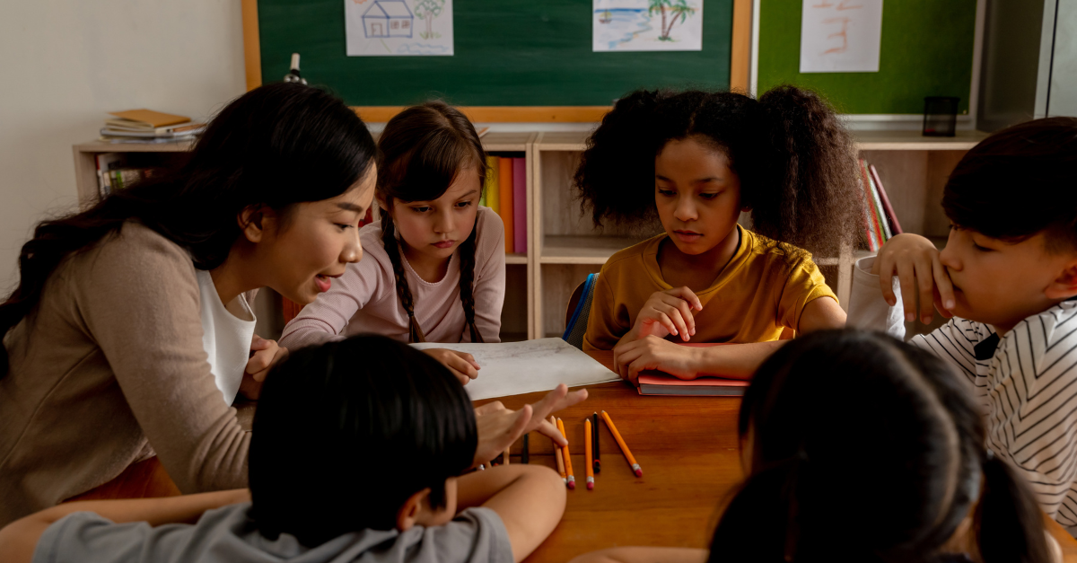 Teacher working with young students together at a table.